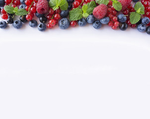 Various fresh summer berries on white background. Ripe raspberries, blueberries, black currants and red currants, mint. Berries at border of image with copy space for text. Top view.