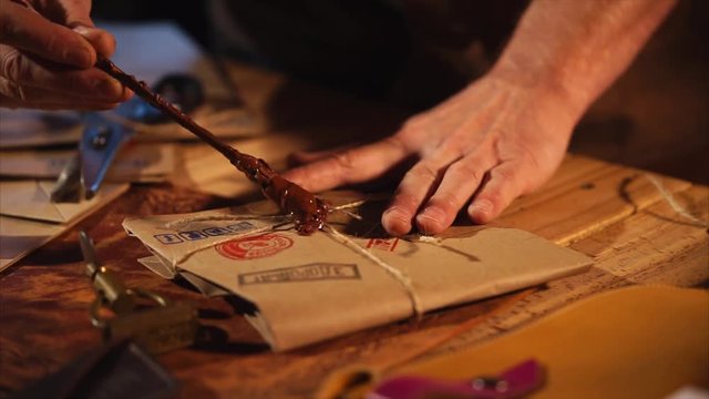 Guy applies some wax on ropes on vintage letter in a studio. He waits for it to cold and seals it very carefully.