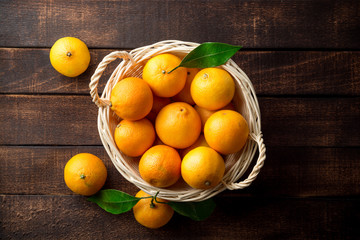 Fresh tangerines in wicker basket on dark wooden background.