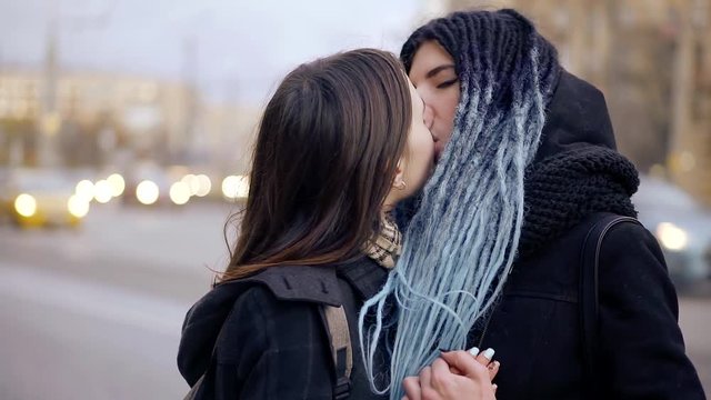 two lesbians kissing on the street, teenagers holding each other's hands during the daytime