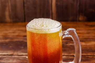 Close up of glass of beer with foam on a wooden table in a dark pub