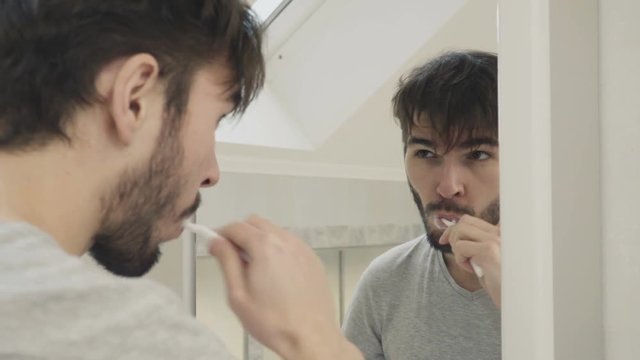 Sleepy guy clean teeth in front of mirror