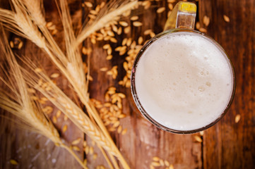 Above view of glass of light beer with foam, with a wheat branch and wheat on a wooden table background
