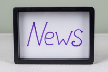 Text word NEWS, in black frame, on white table.