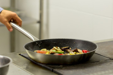 Chef frying vegetables on the gas stove with fire at the kitchen