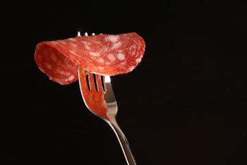 Salami Spain sausage Salchichon on a fork on a dark black background