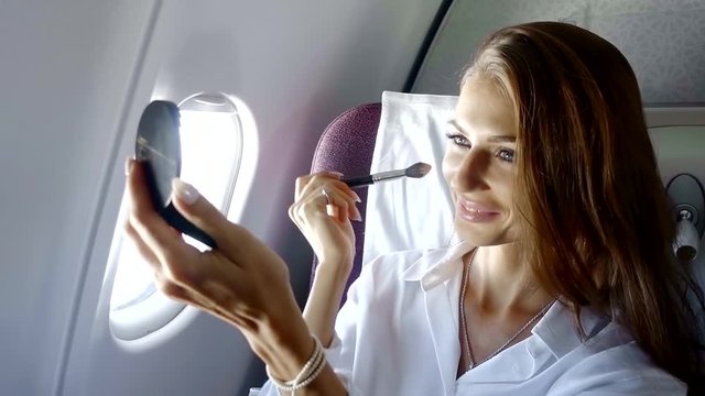 a pretty woman who flies in the plane corrects her makeup, she looks in the pocket mirror