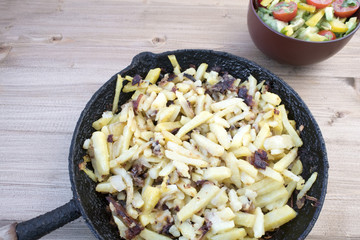 Fried potatoes in a rustic frying pan on a wooden background and vegetable salad.