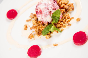 Scoop of ice-cream on roasted nuts decorated with mint and raspberry jelly