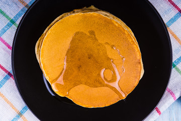 Tasty pancakes with honey on a black plate - top view