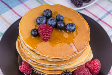Tasty pancakes with honey and blueberries, raspberries and blackberries on a rustic wooden background - top view