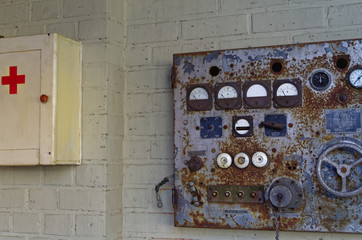 altes historisches Steuergerät einer Maschine mit Potentiometer neben einem Erste-Hilfe Kasten mit rotem Kreuz