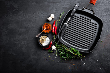 Empty cast-iron grill pan with ingredients for cooking on black background, top view