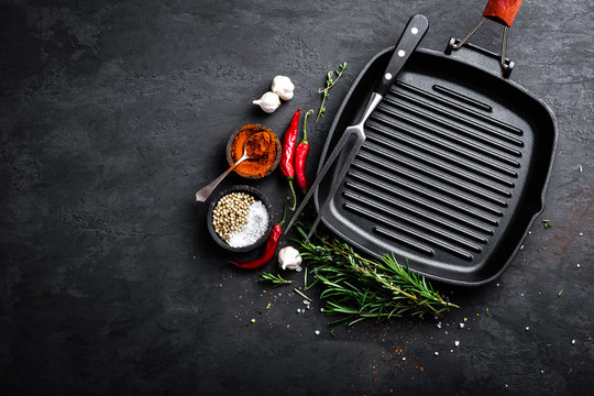 Empty cast-iron grill pan with ingredients for cooking on black background, top view
