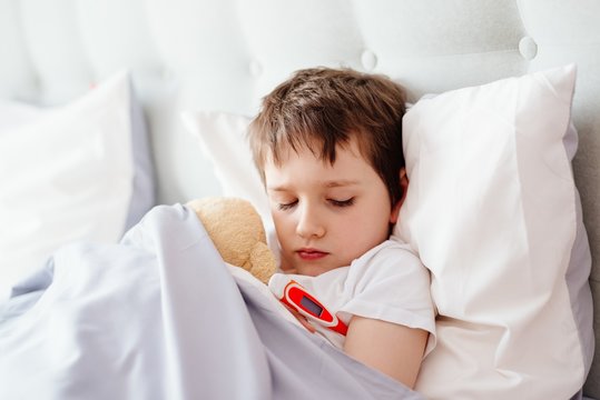 Sick baby boy in bed with a thermometer