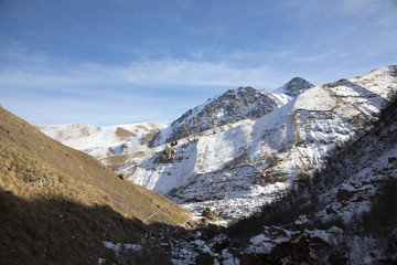 Fototapeta na wymiar Горный пейзаж. Высокие скалы в живописном ущелье, зима, белые облака на синем небе. Дикая природа Северного Кавказа