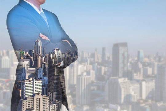 Double exposure of Businessman arms crossed and stand up and cityscape in the morning as business and thinking vision of leader concept.