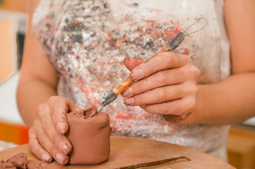 Obraz na płótnie Canvas Close up of woman ceramist hands working with a tool over a sculpture on wooden table in workshop