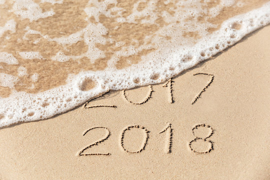 2017 2018 inscription written in the wet yellow beach sand being washed with sea water wave