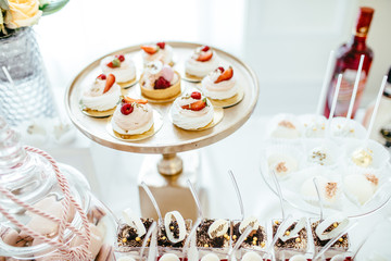 Delicious wedding reception candy bar dessert table full with cakes and sweets and a flower vase with hydrangeas on the background of an exquisite restaurant.