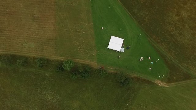The camera takes a white tent on a clearing from above.