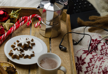 Naklejka na ściany i meble Cozy Christmas at home. Christmas breakfast in bed. Women's feet in warm woolen socks, a cup of coffee and cookies, next to a notebook 