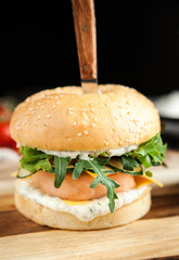 Burger with salmon, French fries and salad on a wooden board