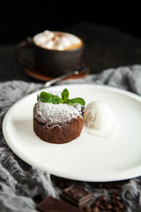 a beautiful serving of chocolate fondant with an ice cream ball, mint and a cup of coffee with marshmallow