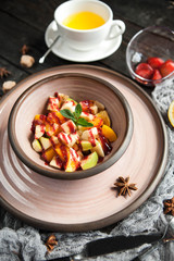 fruit salad with sauce in a ceramic plate with a cup of tea on a wooden background