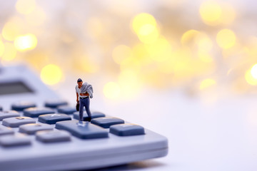 Miniature people: businessman walking on  button of calculator with bokeh