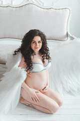 Fototapeta na wymiar Beautiful young pregnant girl with big angel wings in white studio.