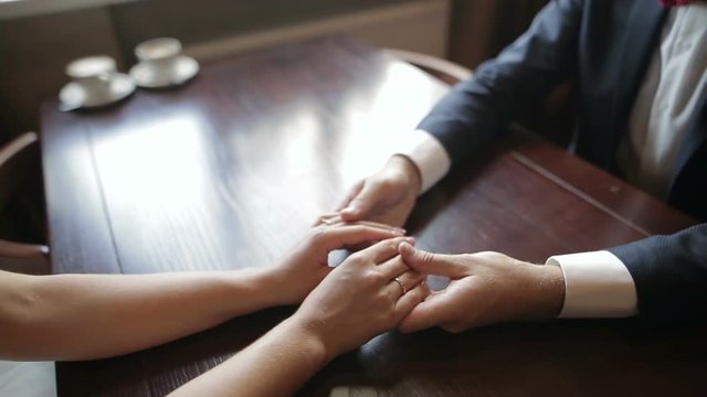 A pair of newlyweds holding hands in a cafe. Close up of human hands.
