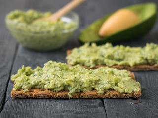 Pate of avocado on a crispy bread on a wooden table.