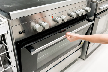 Woman's Hands open the black and silver door of oven machine