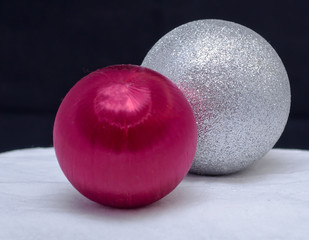 A red Christmas ornament along with a silver glitter one on a white cloth with a black background