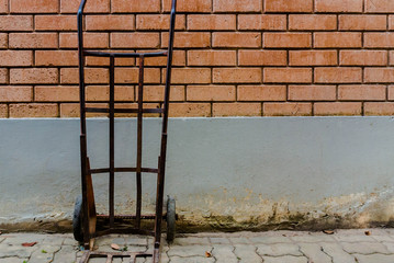 Old wheelbarrow standing a red brick wall interior,Steel hand trolley or sack truck against old brick wall,old steel hand trolley (steel cart) on brick wall