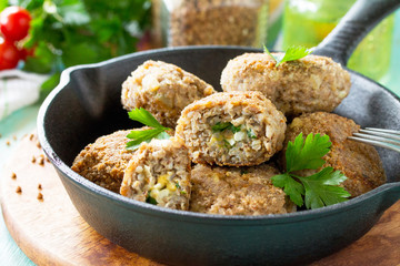 Homemade meatballs with buckwheat and egg stuffing. Cast-iron frying pan with delicious fried cutlets, fresh herbs and vegetables on the kitchen table.