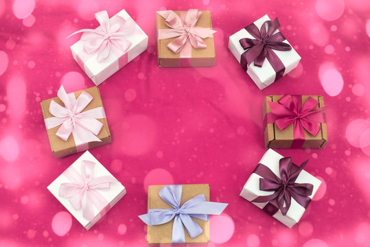 Gift boxes tied with satin coloured ribbon on a pink background.