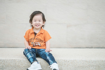 Closeup happy asian kid with smile face sit on marble stone floor and wall textured background with copy space