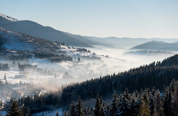 Winter morning landscape. The first shadows of raising sun on mountain slopes, ski resort in a white haze