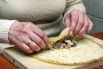 Mother's hands stuff pancakes with minced meat.