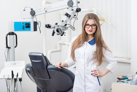 Portrait of attractive female dentist with microscope at the modern dental office. Doctor wearing glasses, white uniform. Dentistry