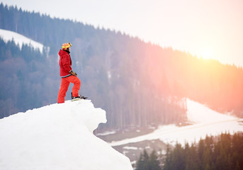 Male snowboarder standing on the top of the snowy hill with snowboard, enjoying sunset. Skiing and...