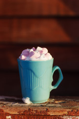 blue mug of drink with whipped cream and marshmallows on wooden background with snow