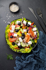 Greek salad in ceramic plate on  black concrete background. Traditional Greek dish. Selective focus. Top view.
