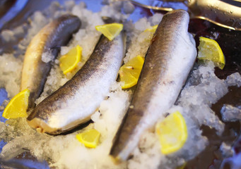Fresh raw sea fish and lemon peces on pan surface.