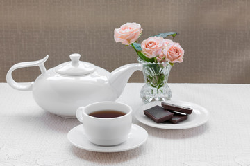teapot, cup, roses and chocolate on a plate