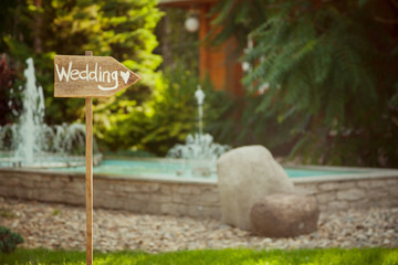 Wedding decor. Wooden plaque with the inscription Wedding. Wedding on a plate green background and a fountain.