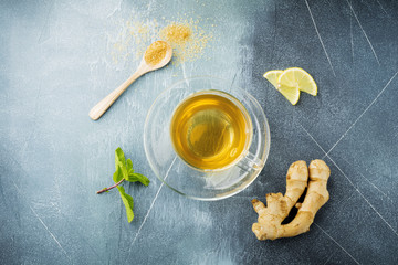 Useful ginger tea with mint, lemon and sugar in a transparent cup on a concrete blue background. Selective focus. Top view.