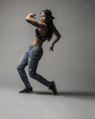 A beautiful black asian woman does an expressive contemporary urban dance move wearing jeans a sports bra and a black baseball cap